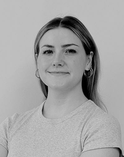 A person with long hair and hoop earrings is smiling slightly. They are wearing a short-sleeved shirt and are posed against a plain background. The image is in black and white.