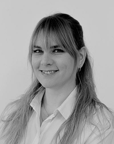 Smiling woman with long hair and bangs, wearing a light-colored collared shirt, looking at the camera in a black and white photo.