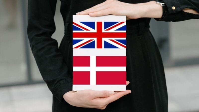 En person i sort outfit holder en bog. Bogens omslag har to flag: Union Jack på den øverste halvdel og det danske flag på den nederste halvdel.