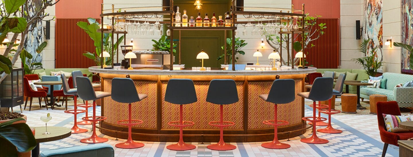 En stilfuld bar med en rund disk, højryggede grå taburetter med røde fødder, hængende glas, flasker på hylder og hyggelige siddepladser - perfekt til at slappe af efter at have nydt rabat på hotelovernatninger i nærheden.