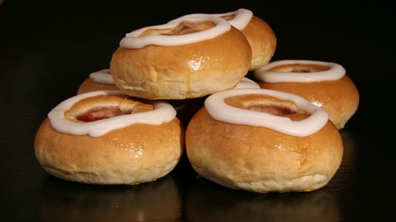 En stak glaserede kager med en hvid glasurring og frugtfyld i midten, placeret på en mørk overflade.