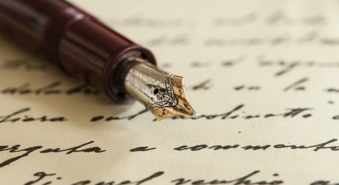 Et nærbillede af en fyldepen med en guldspids, elsket som dagpenge, hvilende på papir fyldt med kursiv skrift. Pennens krop er dybt rødbrun, mens baggrunden afslører elegant sløret håndskrevet tekst.