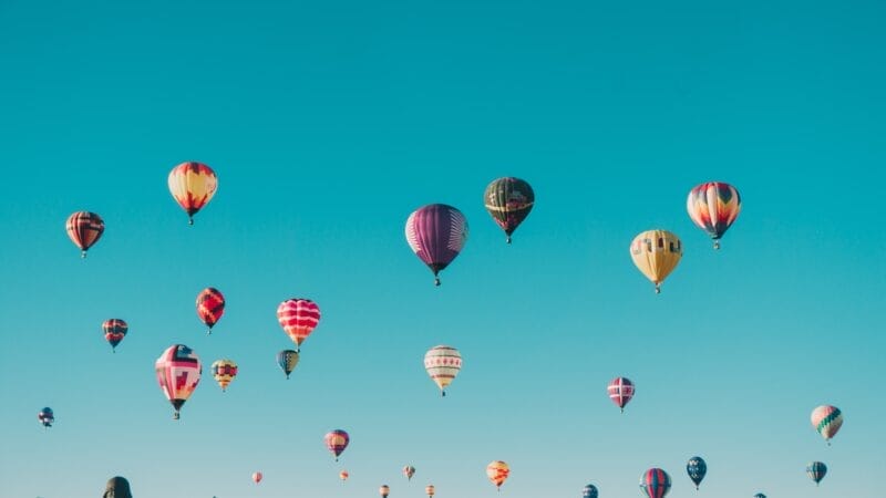 En klar blå himmel fyldt med talrige farverige luftballoner i forskellige størrelser og mønstre, der hver især symboliserer den livlige ånd af et "ungdomsmedlemskab", svæver yndefuldt i forskellige højder.