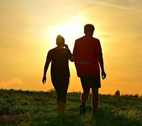 En silhuet af to mennesker, der går på en græsklædt mark ved solnedgang, fremkalder den ro, der ofte mangler i sagsbehandling. Solen kaster et varmt skær og skaber en fredfyldt atmosfære, når de bevæger sig mod horisonten.