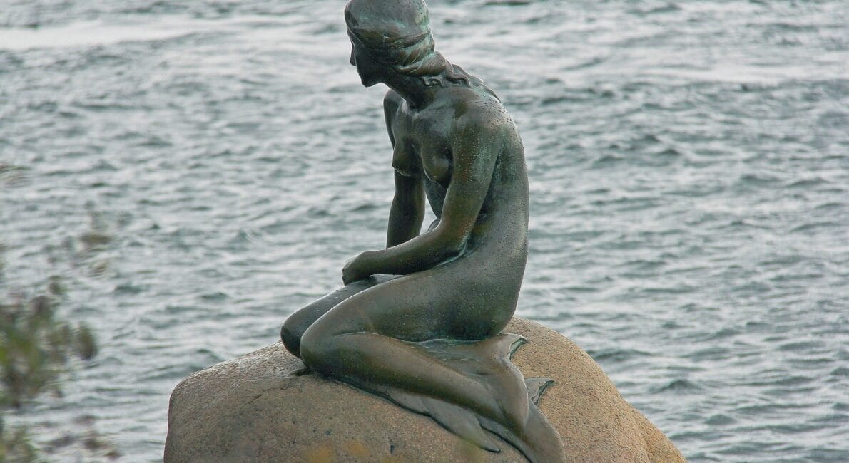 En bronzestatue af en havfrue sidder på en klippe, med udsigt over vandet med et fredfyldt udtryk og halen flyder yndefuldt. Denne rolige scene, omgivet af blide krusninger, fremkalder subtilt den kontemplative natur svarende til at opfylde de strenge "betingelser for bevis for dansk statsborgerskab.