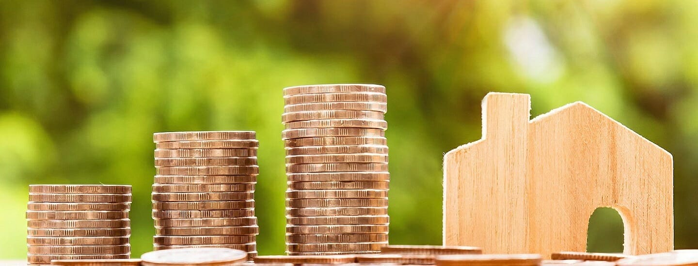 Stabler af mønter er arrangeret i stigende rækkefølge ved siden af et lille træhusudskæring, sat mod en sløret grøn baggrund.