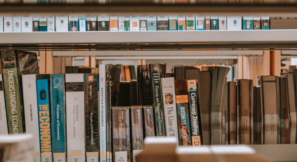 Et nærbillede af en SU-biblioteks reol fyldt med mangfoldige bøger, herunder prominente økonomi- og erhvervstitler. Bindene er tætpakket og viser et rigt billedtæppe af viden og indsigt.